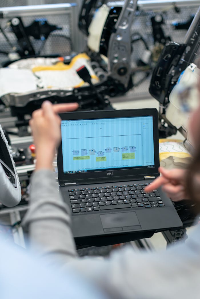 our-journey-03 Engineers using a laptop to analyze software data in an industrial workshop setting.
